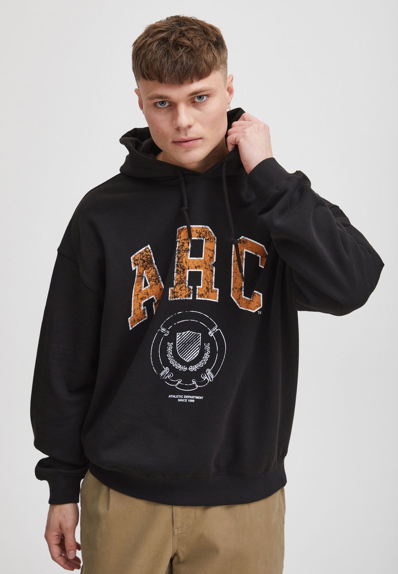 Sudadera con capucha negra hecha de un tejido suave, con letras en relieve naranjas "ARC" y un logotipo gráfico blanco en el centro.