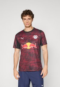 Maillot de sport rouge et noir avec un motif géométrique, doté d'un col rond, de manches courtes et d'un logo Yellow Red Bull bien en vue à l'avant.