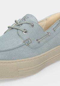 Chaussure bateau en daim bleu clair avec semelle en caoutchouc crème, lacets gris passant dans des œillets métalliques et doublure intérieure beige.