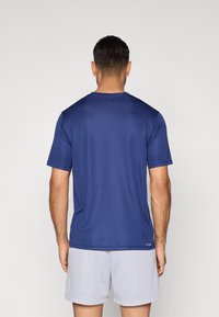 Αθλητική μπλούζα με κοντά μανίκια σε σκούρο μπλε χρώμα, κατασκευασμένη από ελαφρύ υλικό, με στρογγυλή λαιμόκοψη και λεία υφή, εμφανιζόμενη από πίσω.