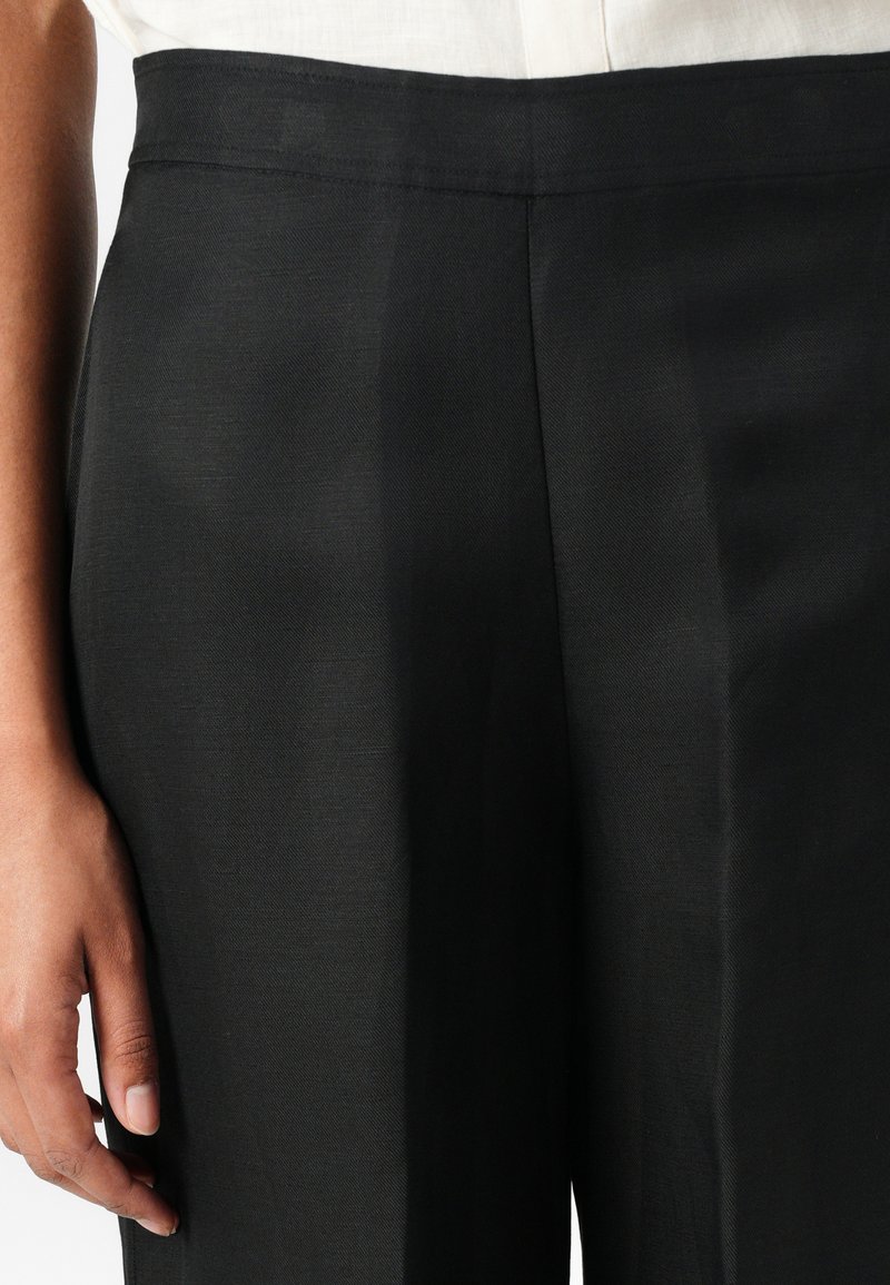 Schwarze, maßgeschneiderte Hose aus einem glatten, leichten Stoff. Verfügt über einen minimalistischen Bund und einen geraden Schnitt mit subtiler Textur.