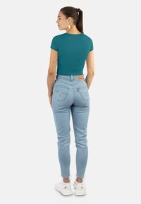 Teal kurzärmeliges, eng anliegendes Oberteil kombiniert mit hellblauen High-Waist Skinny Jeans; weiße Sneaker vervollständigen den Look.