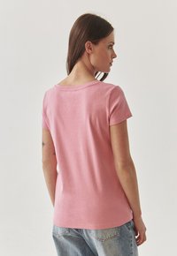 Lyserød bomuld t-shirt med korte ærmer, rund halsudskæring og et afslappet fit, samt lyseblå jeans. Glat tekstur.