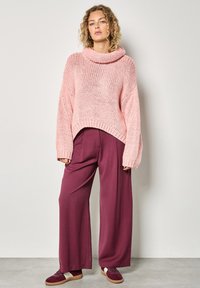 Różowy sweter dzianinowy z wysokim kołnierzem, szerokimi rękawami i luźnym krojem, połączony z bordo szerokimi spodniami i burgundowymi sneakersami.