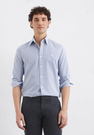Light blue and white striped button-up shirt with a pointed collar, long sleeves rolled up, and a small embroidered logo on the chest.