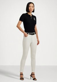 Čierna pletená polokošeľa s krátkym rukávom a logom, doplnená bielymi priliehavými nohavicami a čiernymi sandálmi na vysokom opätku.