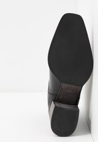 Czarne skórzane buty o spiczastym nosie i pięcie nałożonej z warstw. Podeszwa jest gładka z wytłoczonymi detalami, prezentując czysty, minimalistyczny design.
