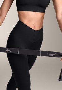 Mustat korkeavyötäröiset leggingsit, joissa on sileä pinta ja tiukka muotoilu, yhdistettynä tumman elastisen vyön kanssa, jossa on harmaa logo ja korostusraja.