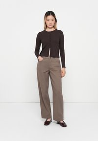 Brun ribbet langermet cardigan med knappelukking, paret med høyt liv, vide beige bukser og glinsende brune loafers.