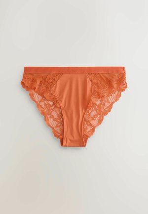 Oranssit bikinimalliset alushousut, joissa on sileä etupaneeli ja kukallinen pitsikoristelu sivuilla ja takana, sekä aaltoilevat reunat.