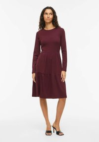 Robe longue mauve à manches longues avec un col rond, un corsage ajusté et une jupe évasée à volants ; fabriquée en tissu doux et extensible.