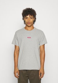 Tricou din bumbac gri cu mâneci scurte, având un logo roșu Levi's centrat pe piept. Guler rotund simplu și croială lejeră.
