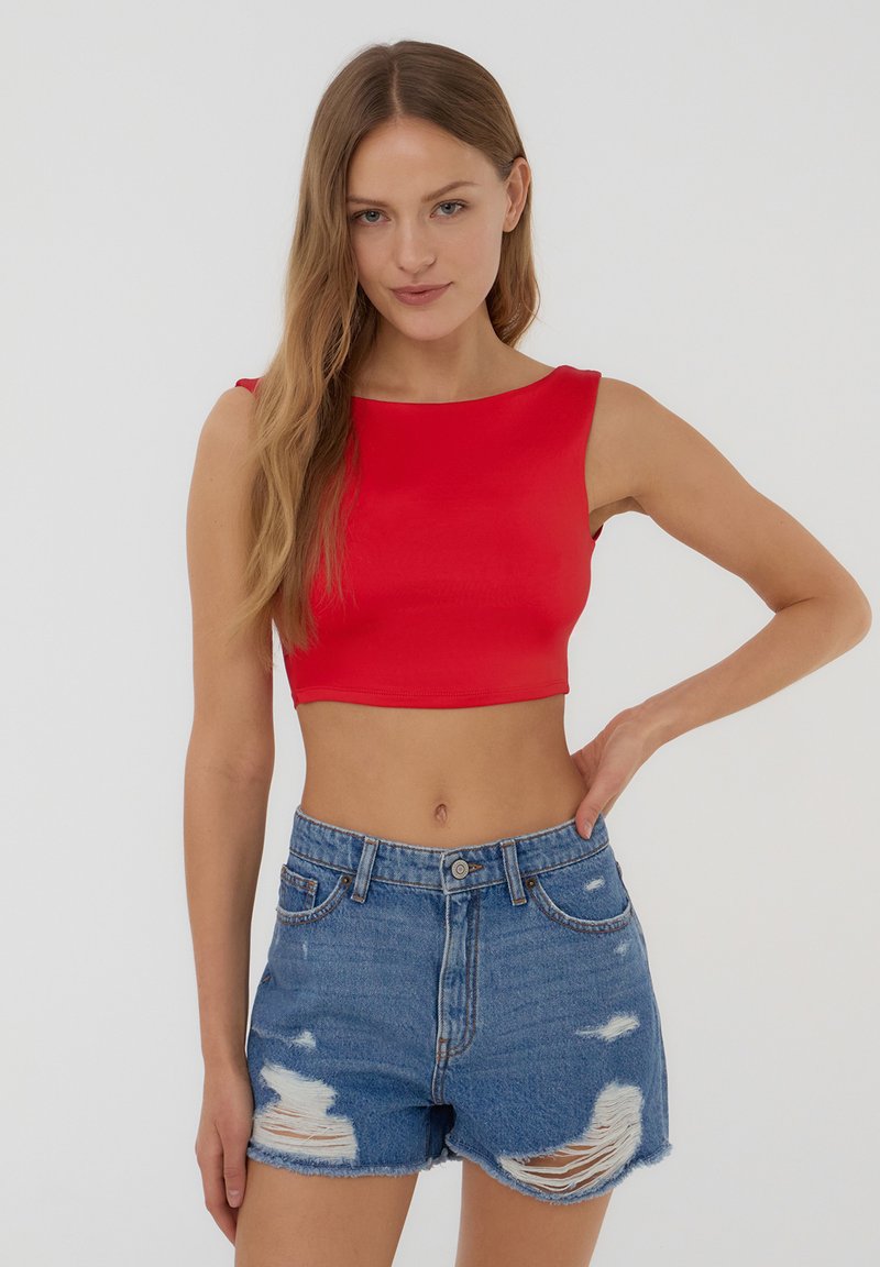 Top corto rosso con scollatura a giro, texture liscia e design senza maniche. Abbinato a pantaloni shorts in denim blu con dettagli strappati.