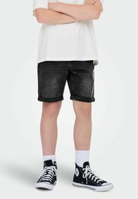 Svarta denimshorts med viker, kombinerade med vita strumpor och svarta hög-top sneakers. T-shirten är enfärgad vit.