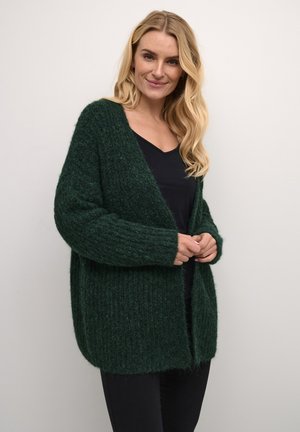 Groene gebreide cardigan met een losse pasvorm, open voorkant, ribbelstructuur en lange mouwen, gecombineerd met een zwarte top en zwarte broek.