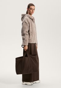 Borsa a tracolla marrone con manici robusti, abbinata a una felpa con cappuccio beige chiaro dalla texture e pantaloni larghi marroni. Design minimalista con un aspetto accogliente.