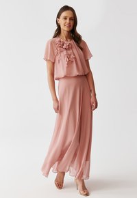 Maxikleid aus sanftem rosa Chiffon, mit einem Überzug, der mit floralen Verzierungen am Ausschnitt versehen ist und einem lässigen, fließenden Schnitt. Betont durch einen dünnen Taillengürtel.