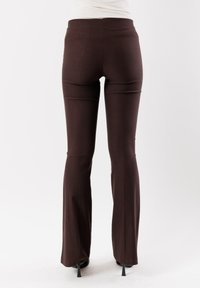 Pantaloni marroni a zampa d'elefante realizzati in tessuto elastico, con una texture liscia e una vita a media altezza, caratterizzati da un design pulito e minimale.