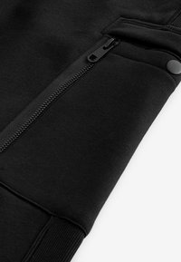 Black sweatshirt cuff featuring a textured fabric, a side zipper with black hardware, and a ribbed hem.