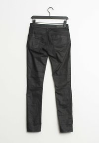 Jeans skinny noirs exposés sur un cintre, dotés d'une texture lisse, de coutures détaillées et de deux poches arrière avec un fini légèrement brillant.