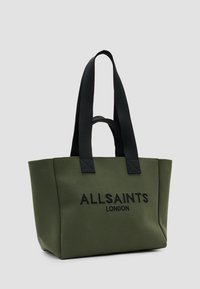 Žalias drobės pirkinių krepšys su juodomis rankenomis, ant priekinės pusės su iškilusiu tekstu "ALLSAINTS LONDON". Kvadratinė forma ir tvirta konstrukcija.