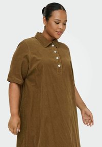 Robe chemise en velours côtelé marron avec col, manches courtes et plastron à cinq boutons. Présente une texture côtelée et une coupe ample et décontractée.