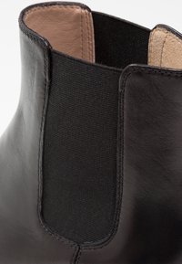 Bottine en cuir noir avec panneau latéral élastique et doublure intérieure beige, gros plan sur la zone supérieure de la cheville.