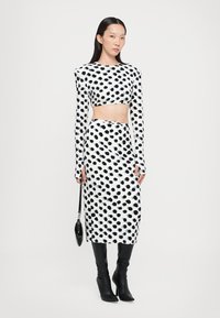 Crop top cu buline albe și negre și fustă creion asortată, mâneci lungi, material neted, asortat cu o geantă de mână neagră și cizme până la genunchi.