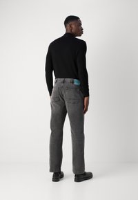 Grijze denim jeans met een rechte snit, twee achterzakken en een blauwe merklabel bij de tailleband. Gepaard met een fitted zwart langemouwen top.