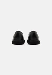 Black leather shoes with a textured surface, rounded toe, and low black sole. Design features stitched seams and minimal accents.