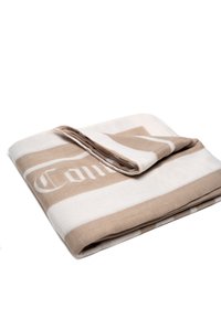 Coperta in cotone con strisce orizzontali beige e bianche, caratterizzata da un design piegato. La superficie è morbida e liscia; include un dettaglio con logo.