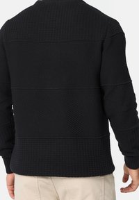 Schwarzer strukturierter Pullover mit Rippenmuster, der horizontale Streifen und einen hohen Kragen aufweist. Weicher Stoff und eng anliegende Bündchen.