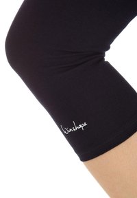 Čierne legíny z elastického materiálu s priliehavým strihom. V blízkosti lemu je viditeľné biele logo „Winshape“. Hladká textúra, dĺžka po lýtka.