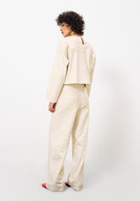 Beige cropped top met lange mouwen en een sleufdetail aan de achterkant, gecombineerd met hooggeplatformde beige wijde broek en rode schoenen.