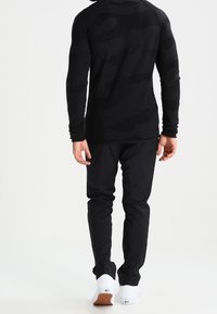 Czarna koszula z długim rękawem z delikatnym wzorem kamuflażu, zestawiona z dopasowanymi czarnymi spodniami i białymi tenisówkami z gumową podeszwą.