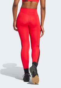 Legging taille haute rouges en tissu extensible, avec des bandes noires sur les côtés, associés à des chaussures de sport noires.