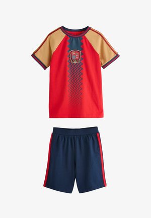 T-shirt de sport à manches courtes rouge et beige avec un motif zigzag bleu et écusson de l'Espagne, associé à un short bleu marine avec des bandes rouges sur les côtés.