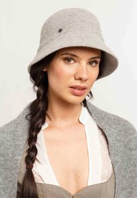 Sivá vlnenná plstená klobúka s okrúhlou korunou a širokým okrajom, s jemným kovovým akcentom na boku. Mäkka textúra a štruktúrovaný tvar.