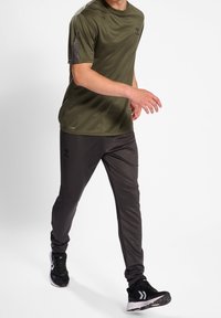 Olivgrön sporttröja och svarta byxor, båda tillverkade av slät, lättviktig tyg. Märkbara detaljer inkluderar mörkgrå accenter och logotyp.