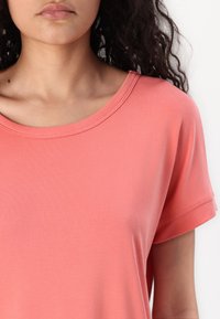 Camicia corta coral a maniche corte con scollo rotondo, realizzata in tessuto morbido ed elastico. Ha una vestibilità comoda con risvolti alle maniche.