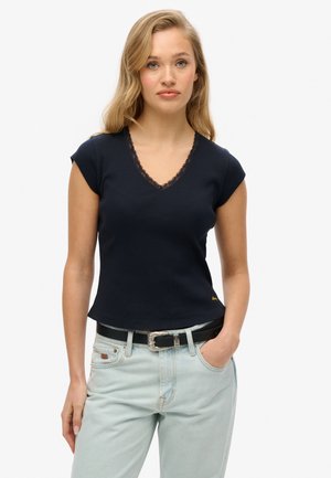Top corto de manga corta en navy con escote en V, que presenta un cuello con borde de encaje y textura acanalada. Combinado con jeans de color azul claro y un cinturón negro.