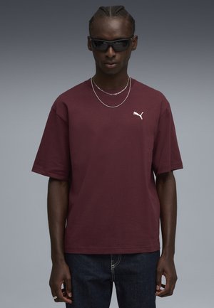 Mørkerød bomulds T-shirt med korte ærmer, rund halsudskæring og hvid Puma-logo på venstre bryst. Bæres med mørke jeans og lagdelte kæder.