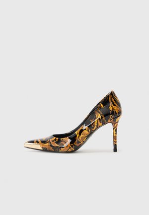 Zapato de tacón alto con punta afilada, superficie negra brillante, adornado con patrones florales dorados y una tapa metálica dorada en la punta.