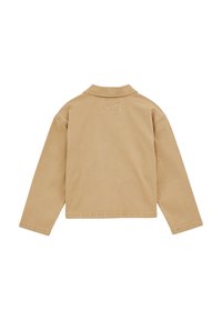 Bež jakna z dolgimi rokavi, ravnim robom in majhno našito pravokotno oznako pod ovratnikom na hrbtu.