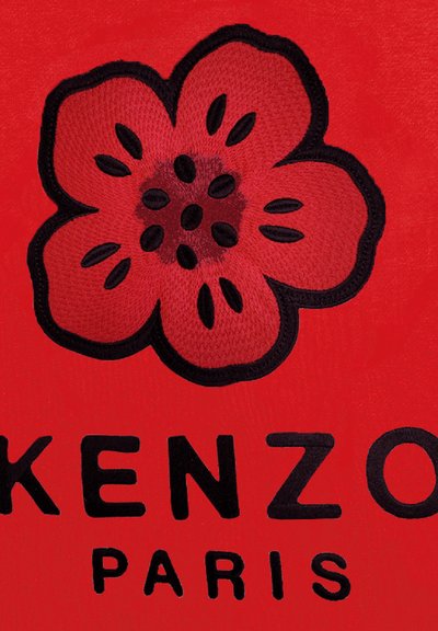 Tissu rouge présentant une fleur brodée en rose avec des contours noirs et des graines foncées, accompagnée du texte noir "KENZO PARIS."