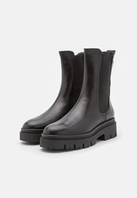 Botines de cuero negro al tobillo con paneles elásticos en los laterales, punta redondeada y una suela de goma negra gruesa con un patrón de textura.