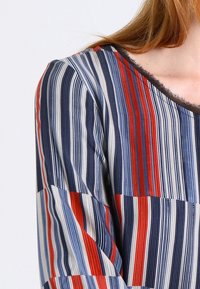 Maglietta a righe con strisce blu navy, rosse e crema. Realizzata in tessuto morbido, con scollatura rotonda e maniche corte. Bordo testurizzato.