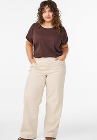 Hellbeige weite Hose mit hoher Taille und Taschen, kombiniert mit einem braunen T-Shirt mit kurzen Ärmeln. Glatte Stoffstruktur und lässige Passform.