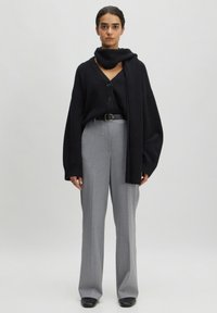 Schwarzer, übergroßer Cardigan mit Knöpfen, über einem schwarzen Strickoberteil getragen, kombiniert mit grauen, hoch taillierten Hosen und einem passenden schwarzen Schal.