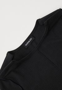 Schwarzes geripptes Oberteil mit rundem Ausschnitt, das ein schlichtes Design und genähte Akzente aufweist. Enthält ein Logonetikett am Ausschnitt.